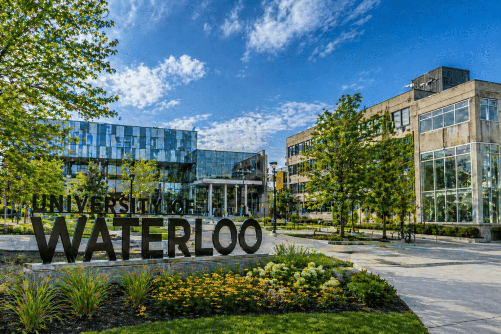 modern university campus with glass buildings, landscaped garden, and walkway under blue sky.